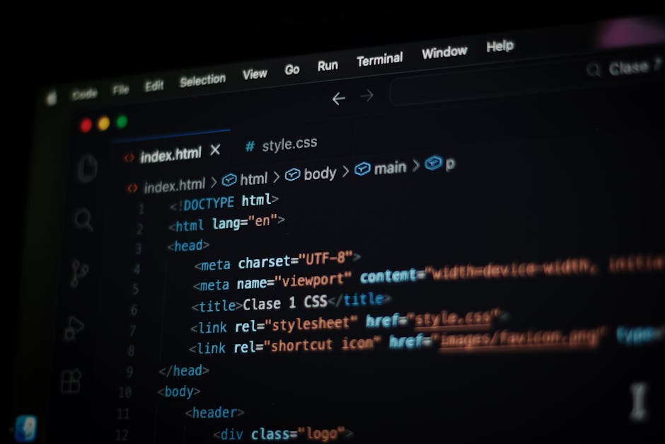 This image shows a person's hands typing on a laptop keyboard, with the screen displaying lines of computer code set against a dark background. The laptop is placed on a smooth, reflective surface, an
